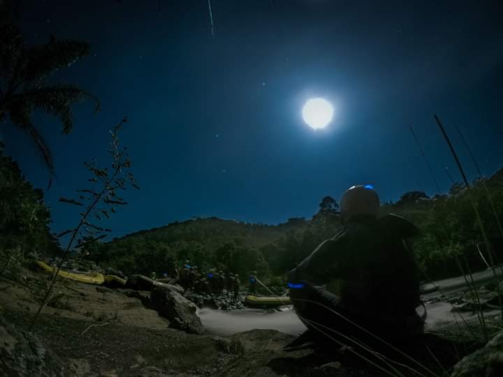 Guia de capacete observando o rio iluminado pela lua, com os botes ao fundo