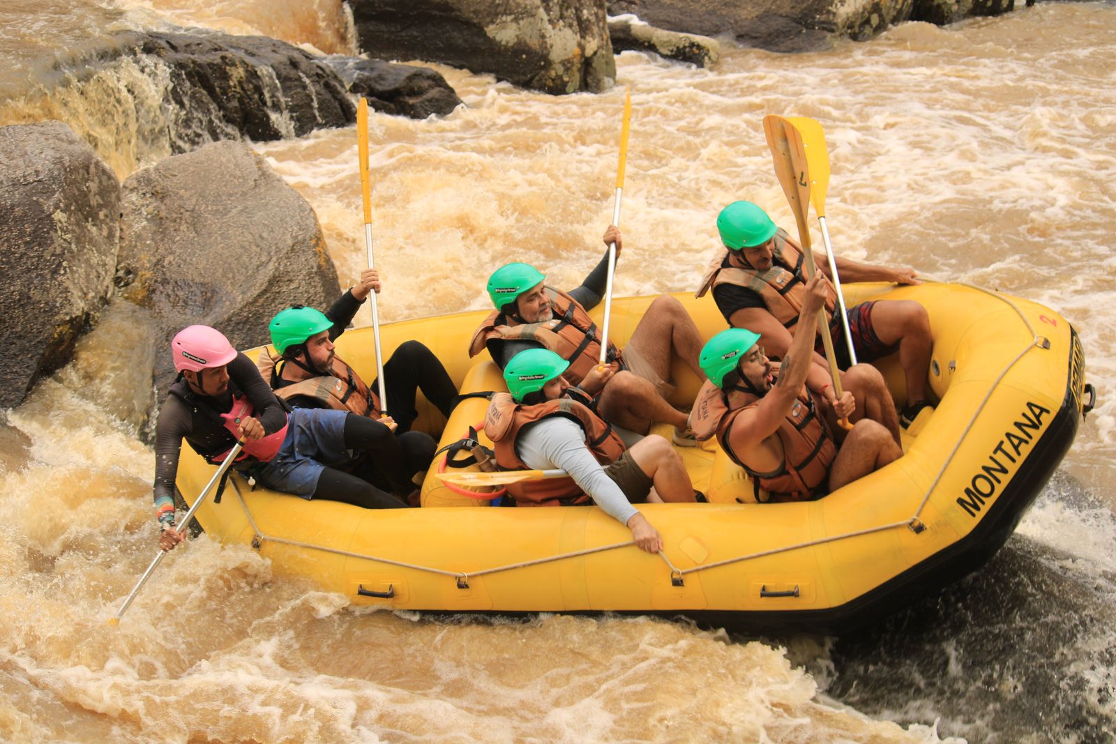 Bote da Montana com turma de capacete verde descendo corredeira entre pedras no Palmeiras