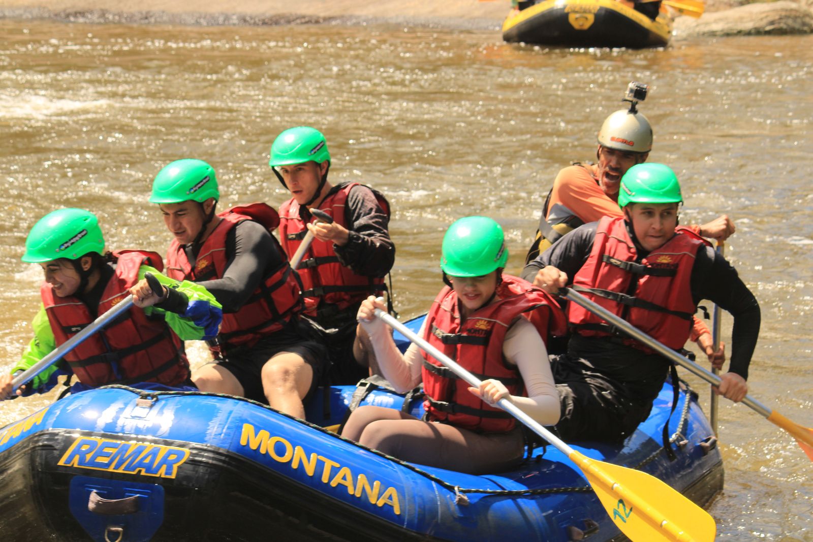 Grupo de capacete verde e colete vermelho remando junto no bote da Montana